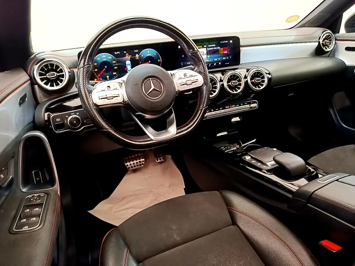Intérieur noir de la Mercedes CLA 200 d AMG Line 2021, vue cockpit avec volant cuir, écran tactile et aérateurs ronds chromés.