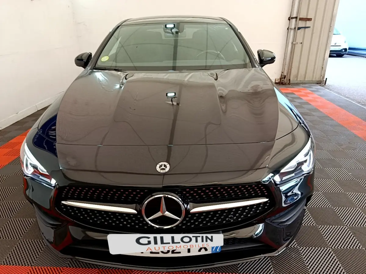 Vue frontale d'une Mercedes CLA 200 d AMG Line noire avec calandre étoilée et phares LED allumés dans un garage.