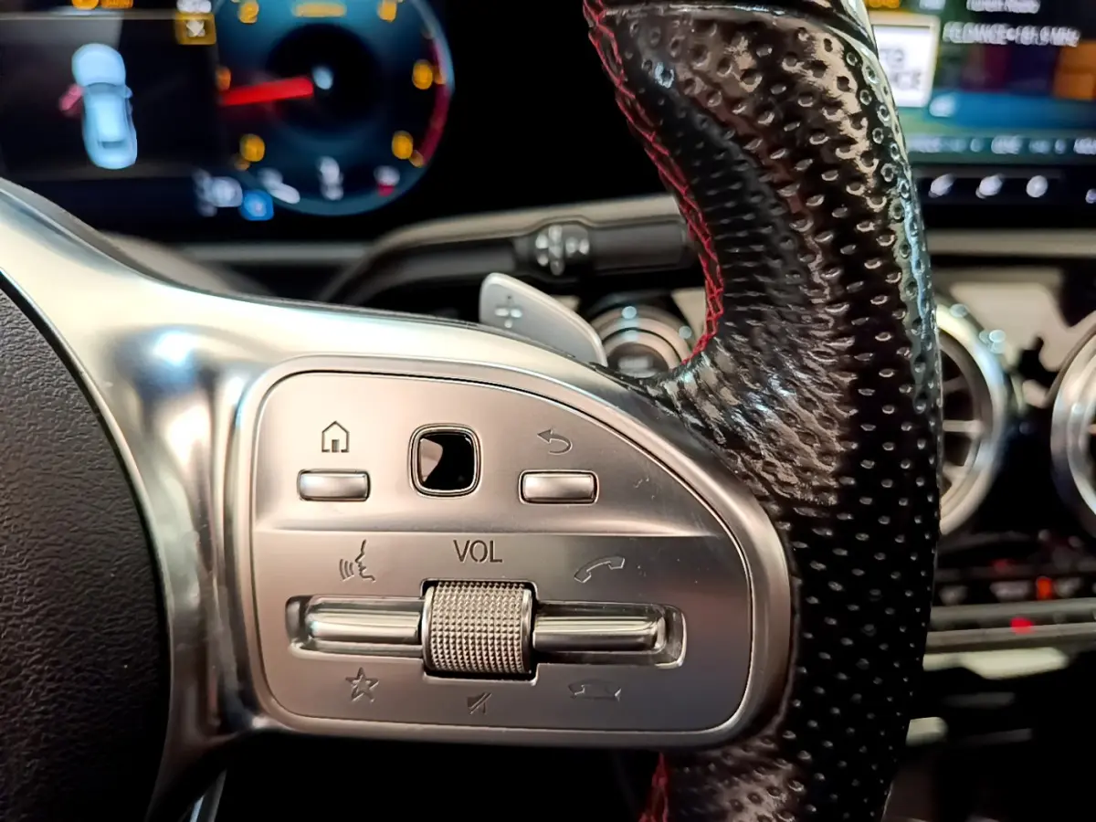 Gros plan sur la commande de volume en aluminium et cuir perforé du volant à droite d'une Mercedes CLA 200 d AMG Line noire.