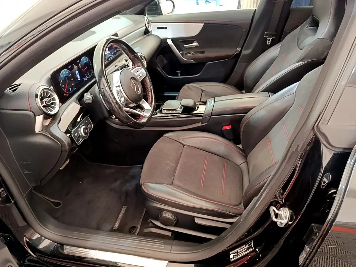 Intérieur avant droit de la Mercedes CLA 200 d AMG Line 2021 noir, sièges sport avec surpiqûres rouges et tableau de bord digital.