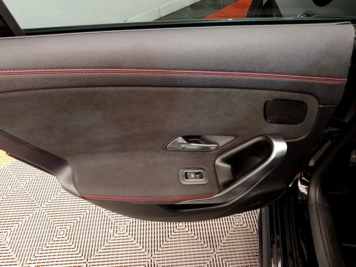 Gros plan sur la porte intérieure côté gauche noire avec surpiqûres rouges et poignée métal d'une Mercedes CLA 200 d AMG Line 2021.