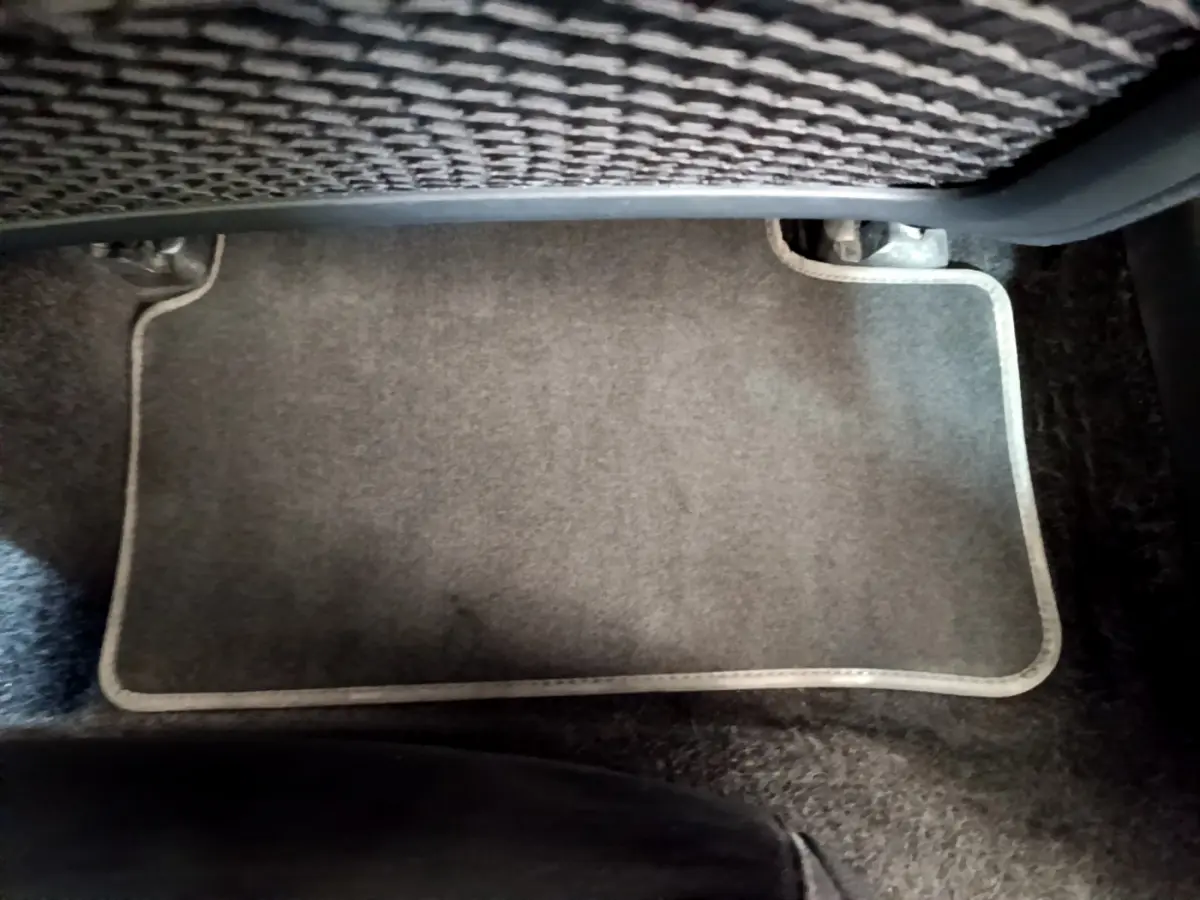 Tapis de sol gris clair sous le siège arrière d'une Mercedes CLA 200 d AMG Line noir, vue rapprochée intérieure.