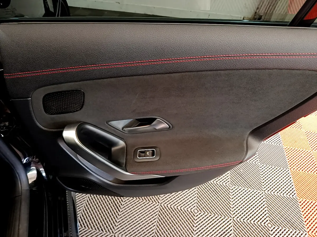 Gros plan sur la porte intérieure côté gauche d'une Mercedes CLA 200 d AMG Line noire avec surpiqûres rouges.