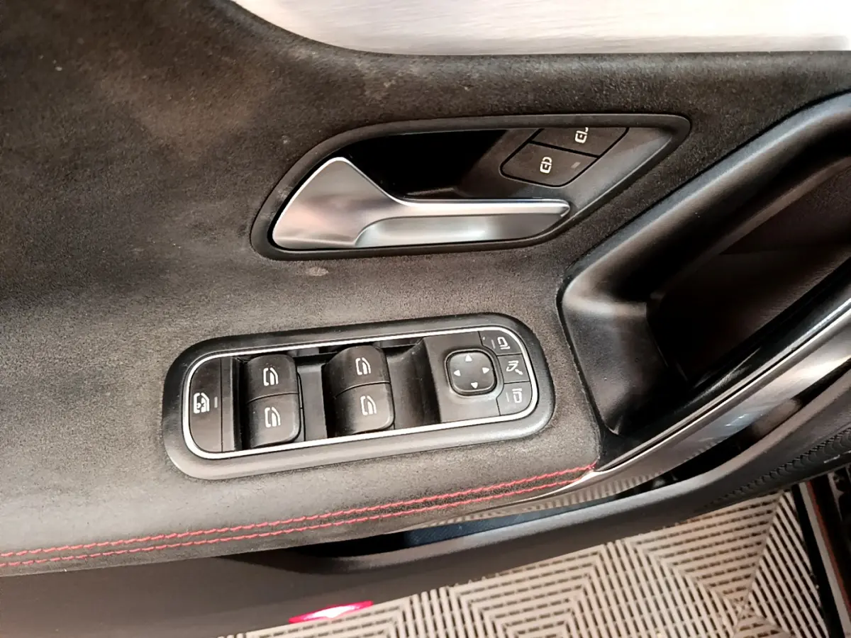 Gros plan sur la garniture intérieure noire de la porte côté conducteur avec commandes de vitres et poignée alu.