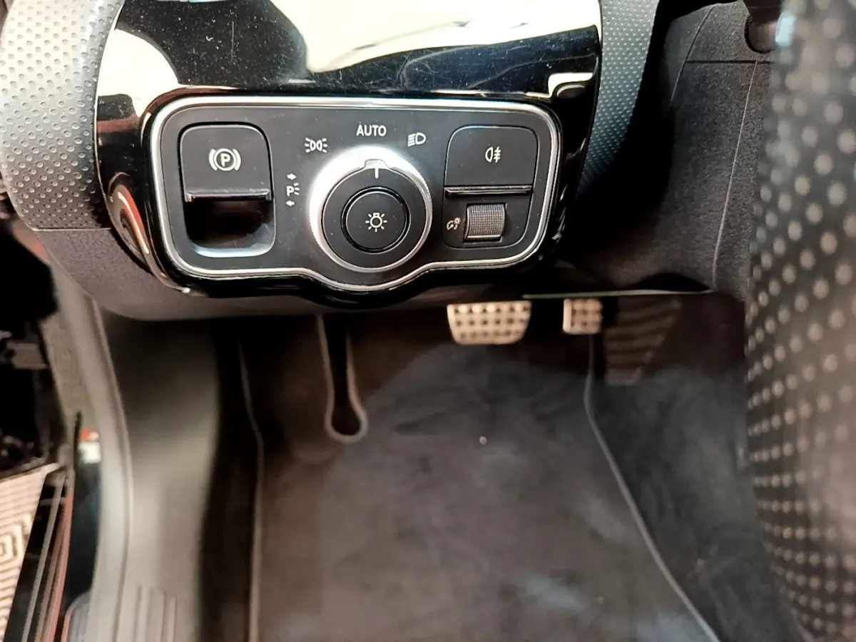 Vue rapprochée du panneau de commande des phares et frein à main électrique côté gauche d'une Mercedes CLA 200 d AMG Line noire.