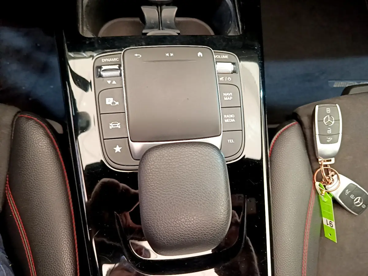 Gros plan sur la console centrale noire brillante de la Mercedes CLA 200 d AMG Line avec pavé tactile et clé Mercedes posée à côté