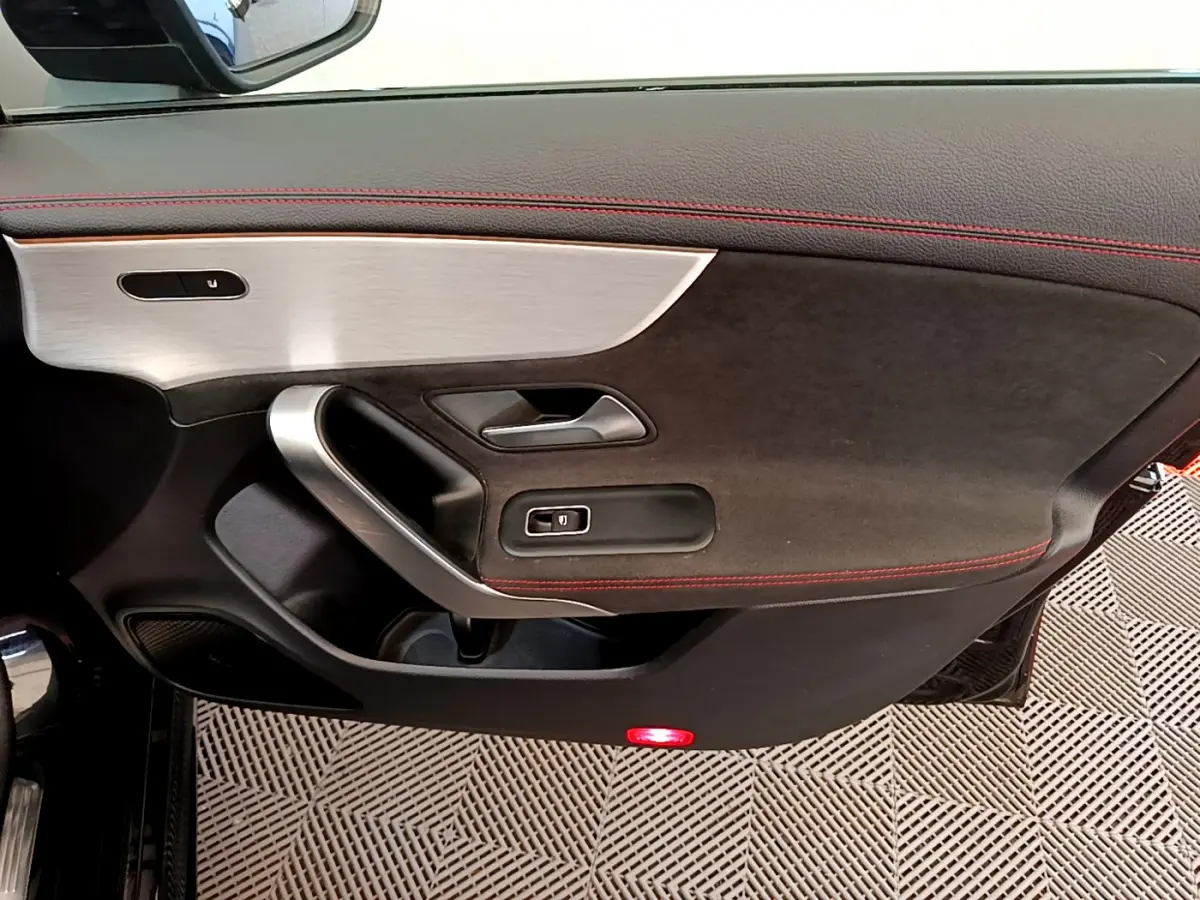 Gros plan sur la porte intérieure côté gauche de la Mercedes CLA 200 d AMG Line noire avec surpiqûres rouges et insert aluminium.