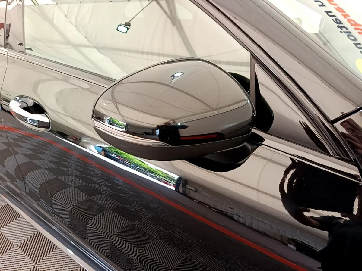 Gros plan sur le rétroviseur côté gauche noir brillant d'une Mercedes CLA 200 d AMG Line 2021 avec reflet du plafond.