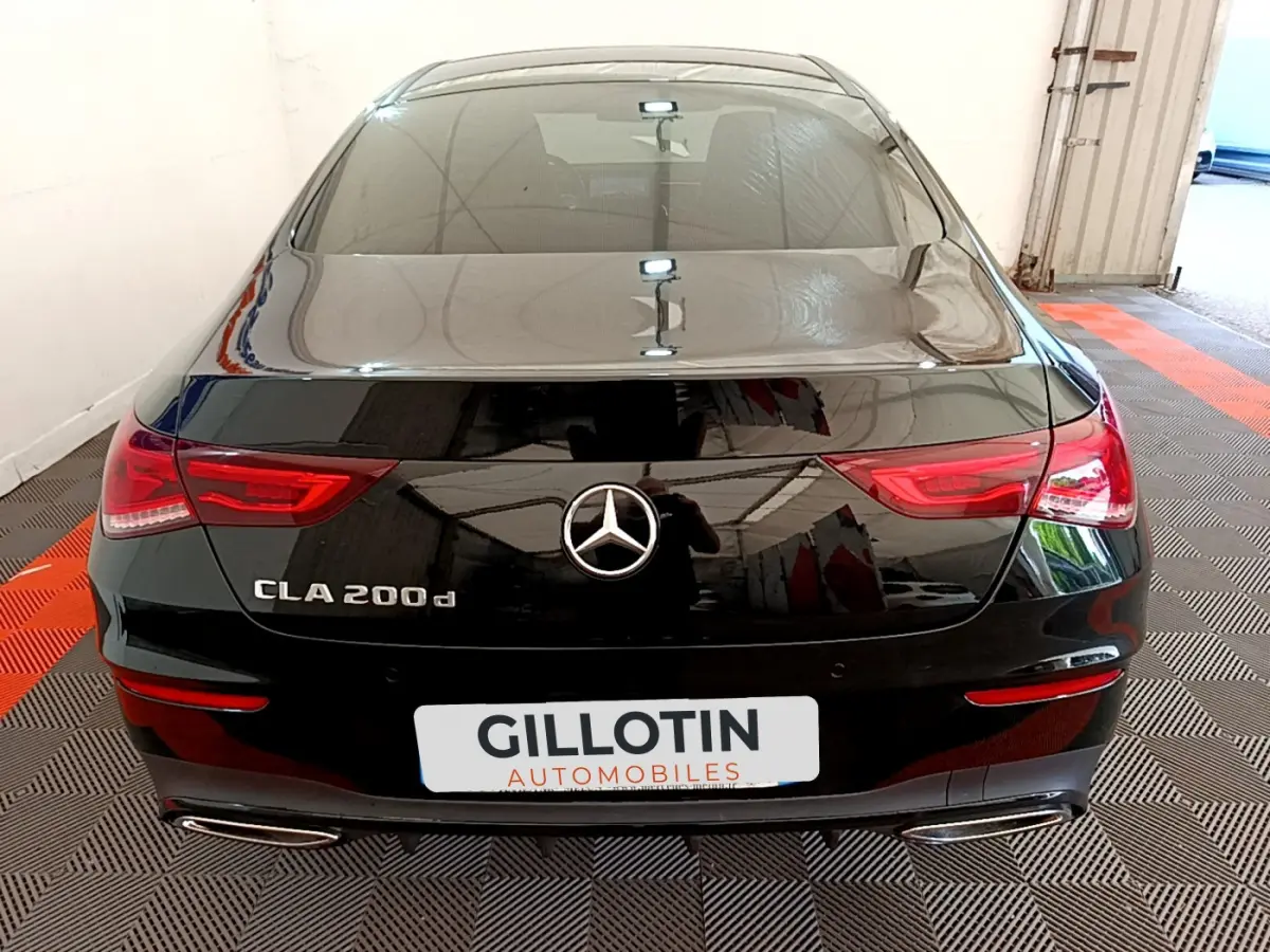 Vue arrière d'une Mercedes CLA 200 d AMG Line noire stationnée dans un garage avec feux LED allumés.