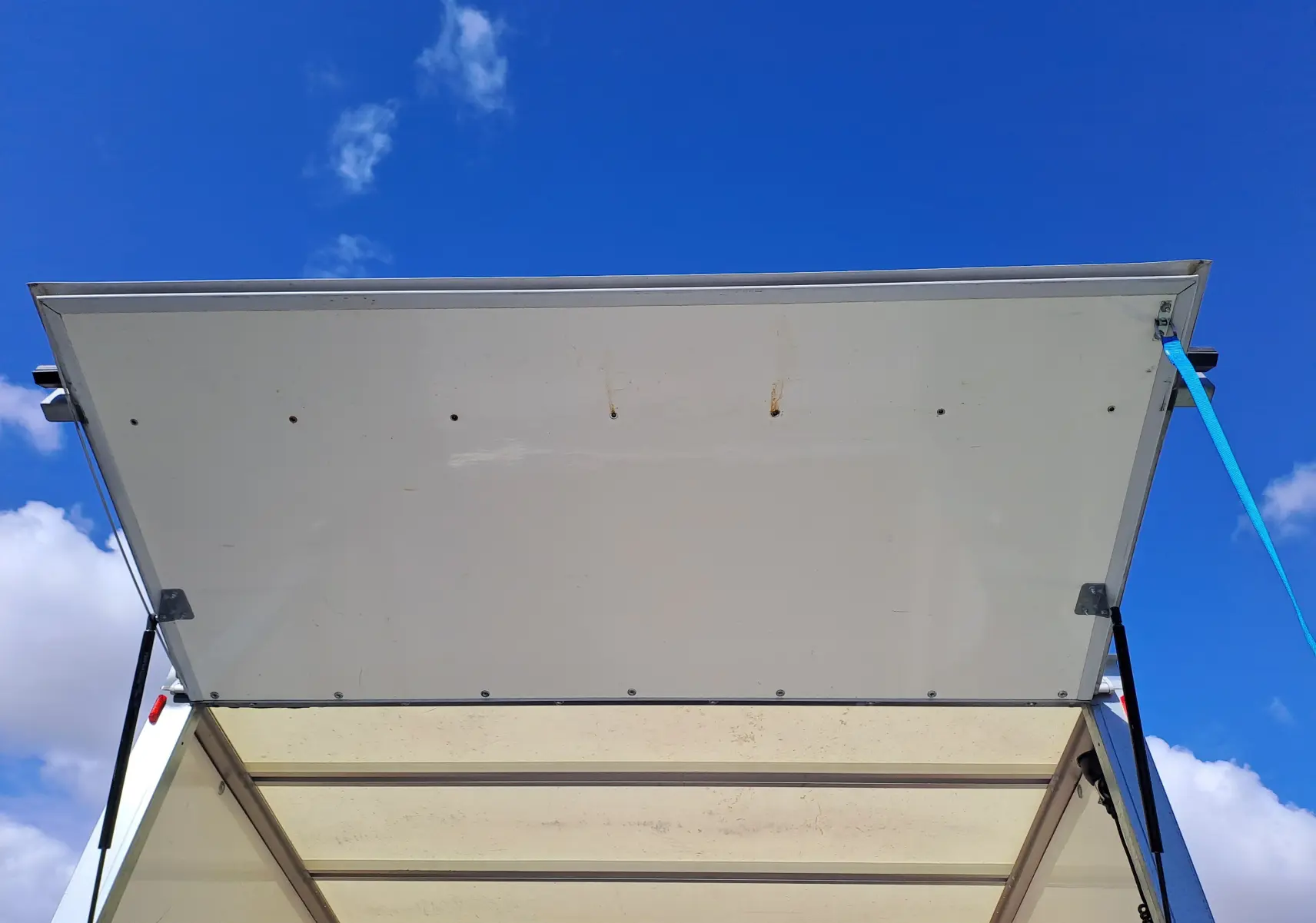 Vue de dessous de la porte arrière blanche ouverte d'un Nissan Interstar Châssis Cabine 2024, ciel bleu en arrière-plan.