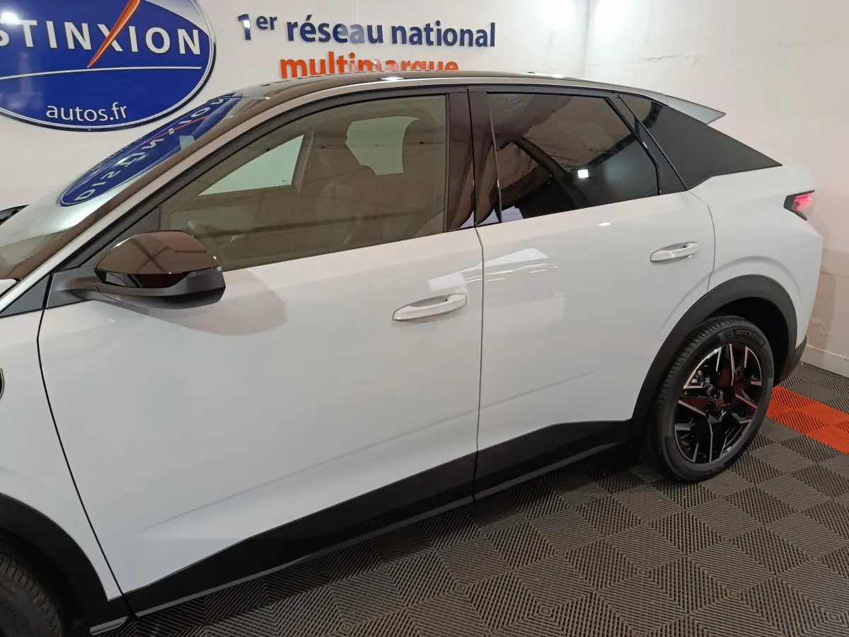 Profil côté gauche du Peugeot 3008 blanc hybride 2025 avec vitres teintées et jantes noires en intérieur showroom.