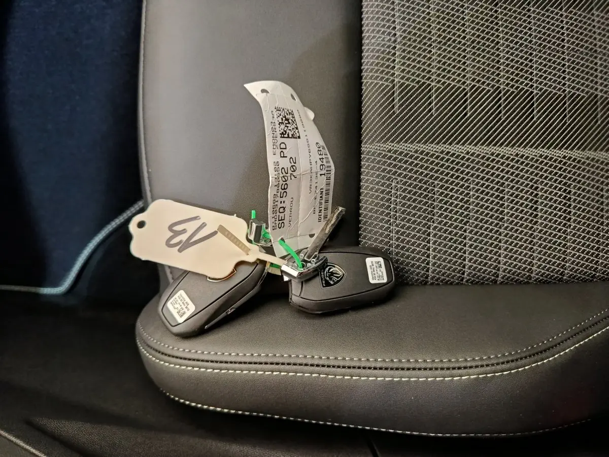 Clé de voiture Peugeot posée sur un siège avant noir avec tissu à motifs gris et coutures blanches visibles