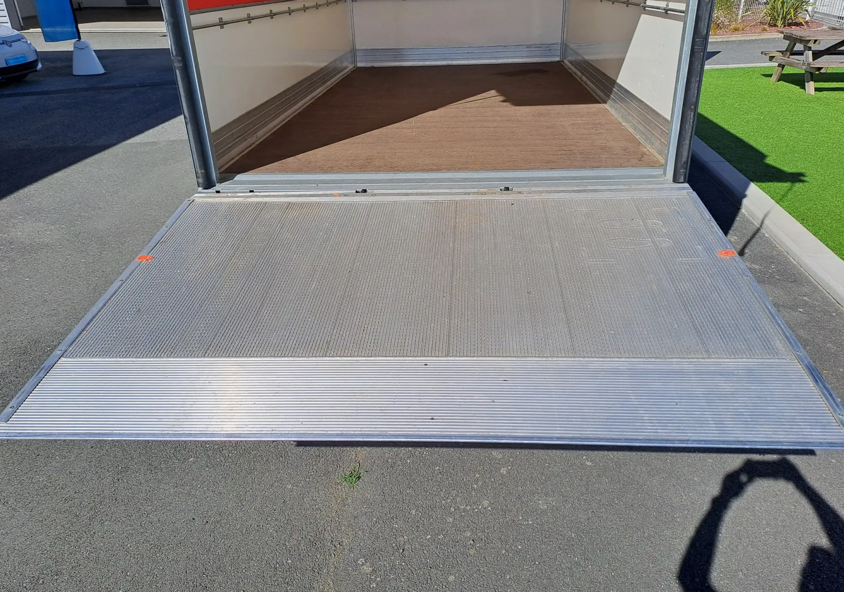 Vue arrière rapprochée du Nissan Interstar blanc 2024, montrant la benne ouverte avec plancher en bois et rampe métallique.
