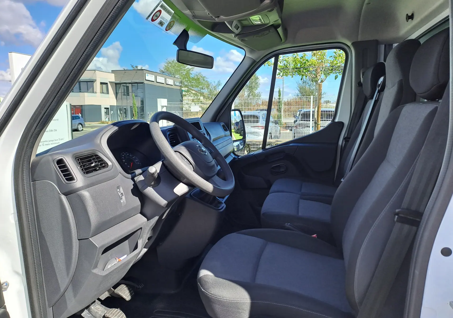 Vue intérieure côté conducteur du Nissan Interstar blanc 2024, montrant le tableau de bord et les sièges en tissu gris.