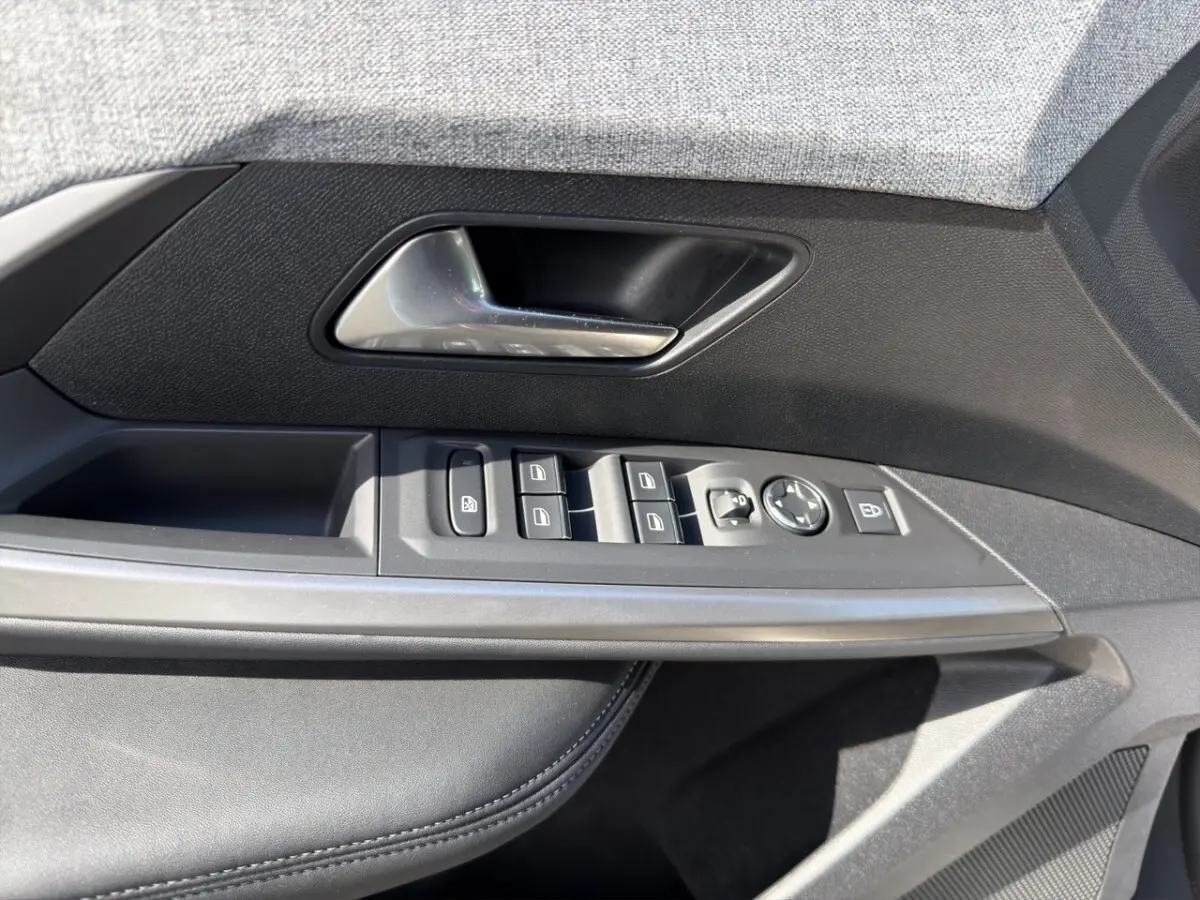 Gros plan sur la porte avant gauche du Peugeot 5008 gris foncé, montrant les commandes électriques des vitres et rétroviseurs.
