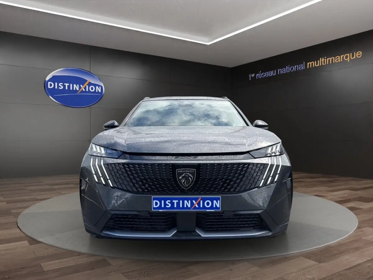 Vue frontale d’un Peugeot 5008 gris foncé avec calandre noire et feux LED distinctifs en forme de griffes.
