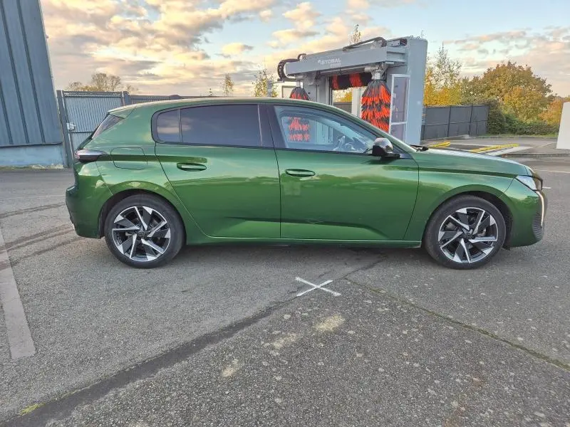 Profil côté gauche d'une Peugeot 308 2023 vert olivine avec jantes alliage et vitres arrière surteintées.