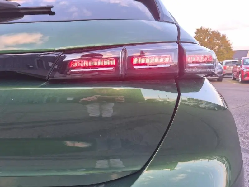 Gros plan sur le feu arrière droit rouge d'une Peugeot 308 2023 vert olivine, avec reflets sur la carrosserie.