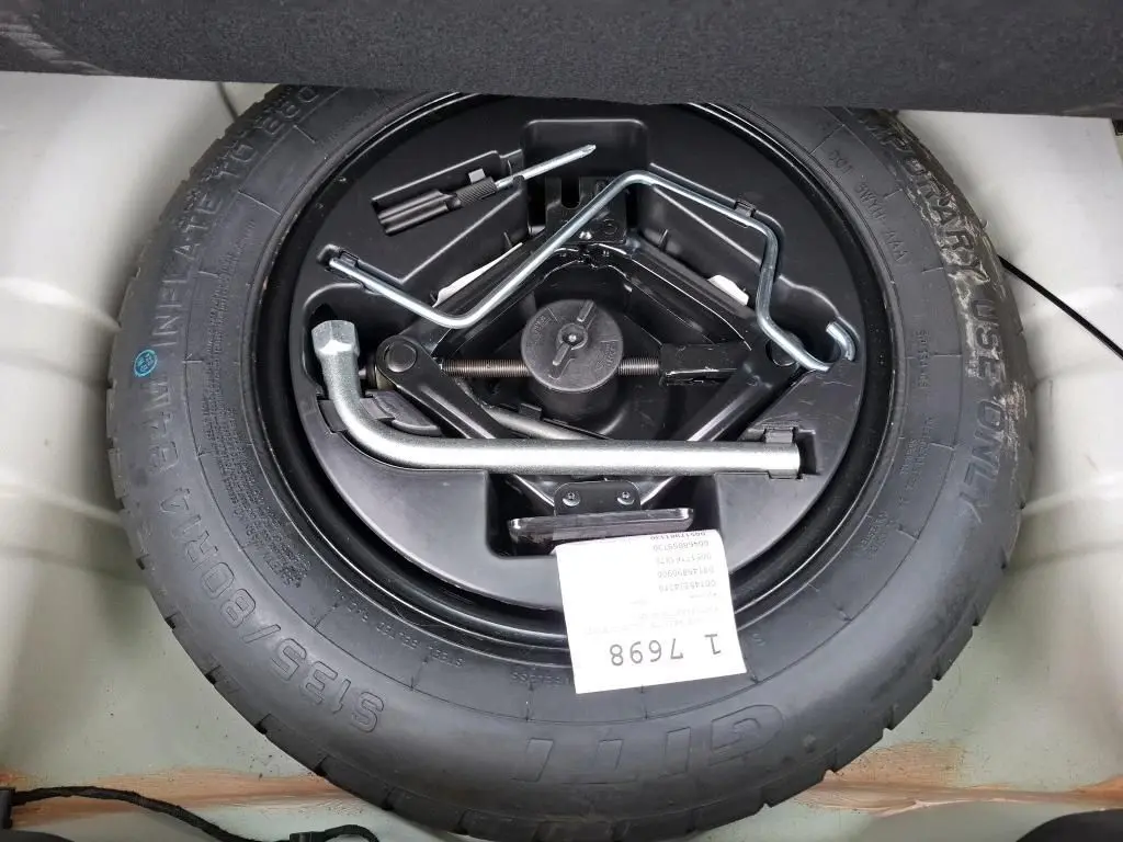 Vue plongeante sur la roue de secours noire avec outils de changement, dans le coffre d'une FIAT 500 blanche 2022.