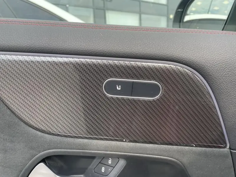 Détail de la garniture intérieure en fibre de carbone avec commande de siège chauffant sur porte côté gauche d'un Mercedes GLA rouge métal 2022 AMG-LINE.