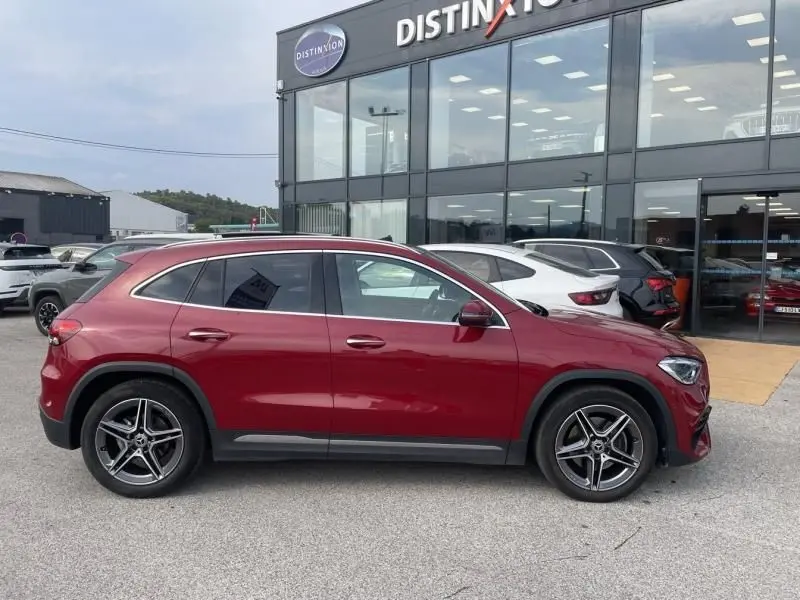 Profil côté gauche d'un Mercedes GLA 200 D AMG-Line rouge métal 2022 garé devant un showroom automobile.