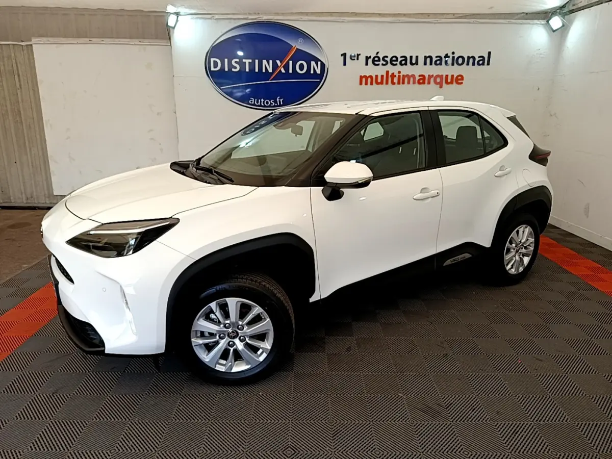 Toyota Yaris Cross blanc vue 3/4 avant droit en intérieur, avec jantes alliage et protections noires contrastées.