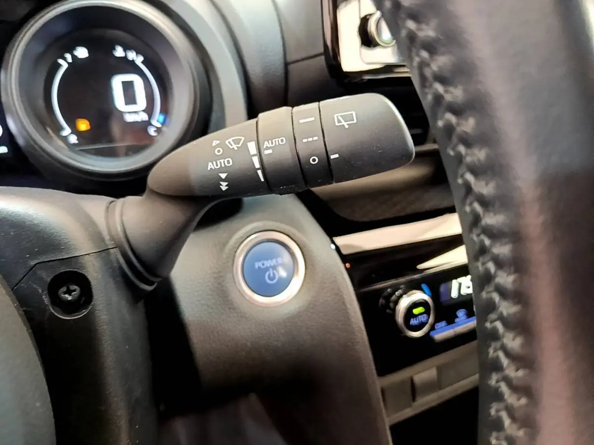 Gros plan sur la commande d'essuie-glace et le bouton Power dans l'habitacle noir de la Toyota Yaris Cross blanche.