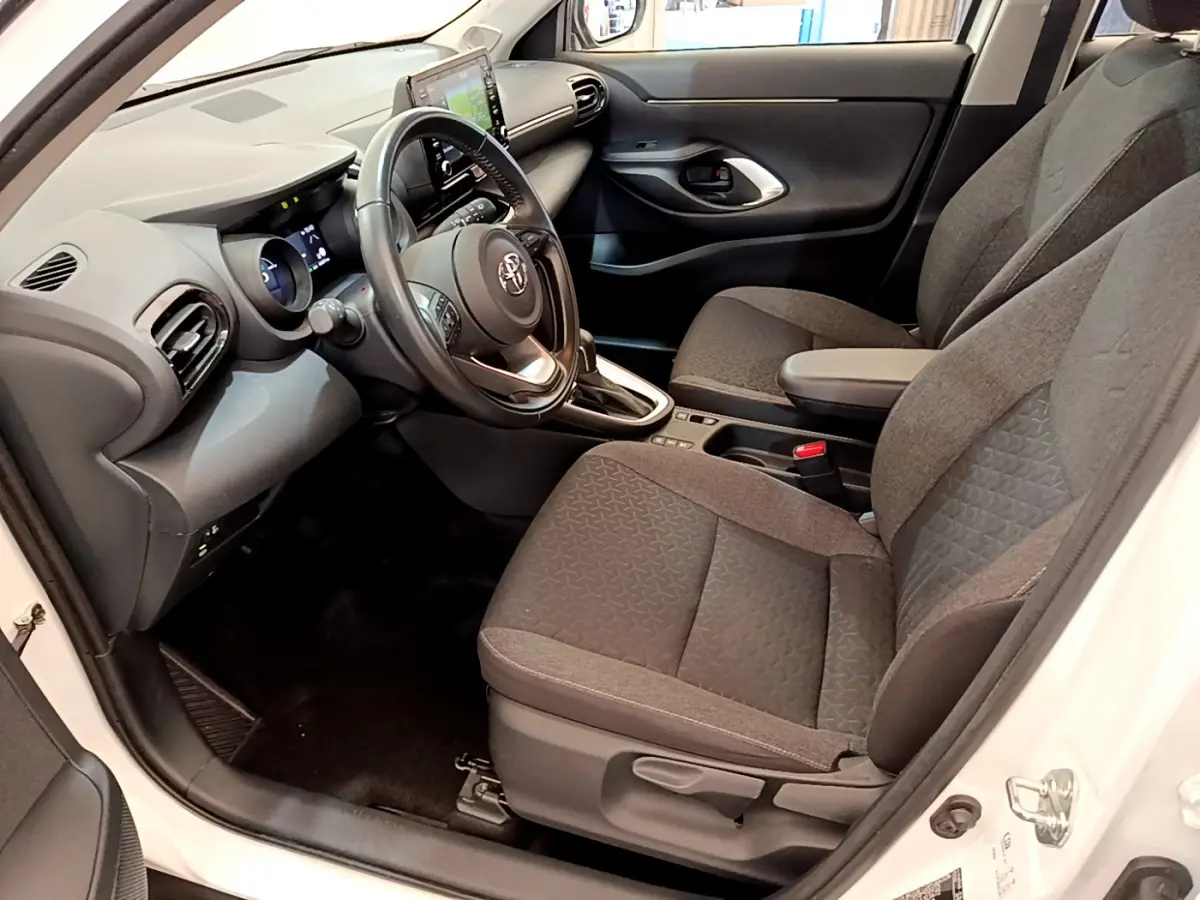 Vue intérieure côté conducteur du Toyota Yaris Cross 2022 blanc, avec sièges tissu gris et tableau de bord moderne.