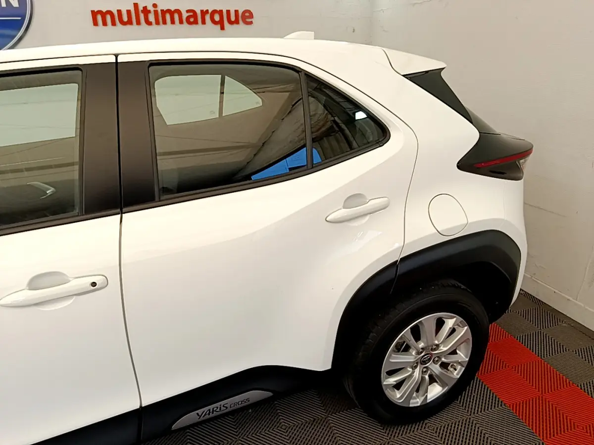 Vue côté droit arrière du Toyota Yaris Cross blanc avec jantes alliage et logo Yaris Cross sur bas de caisse.