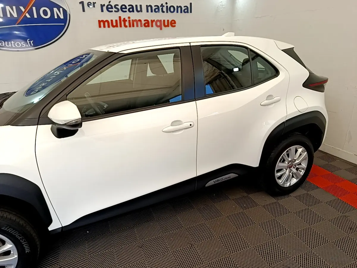 Profil côté gauche d'une Toyota Yaris Cross blanche 2022 avec logo sur bas de caisse, en intérieur showroom.