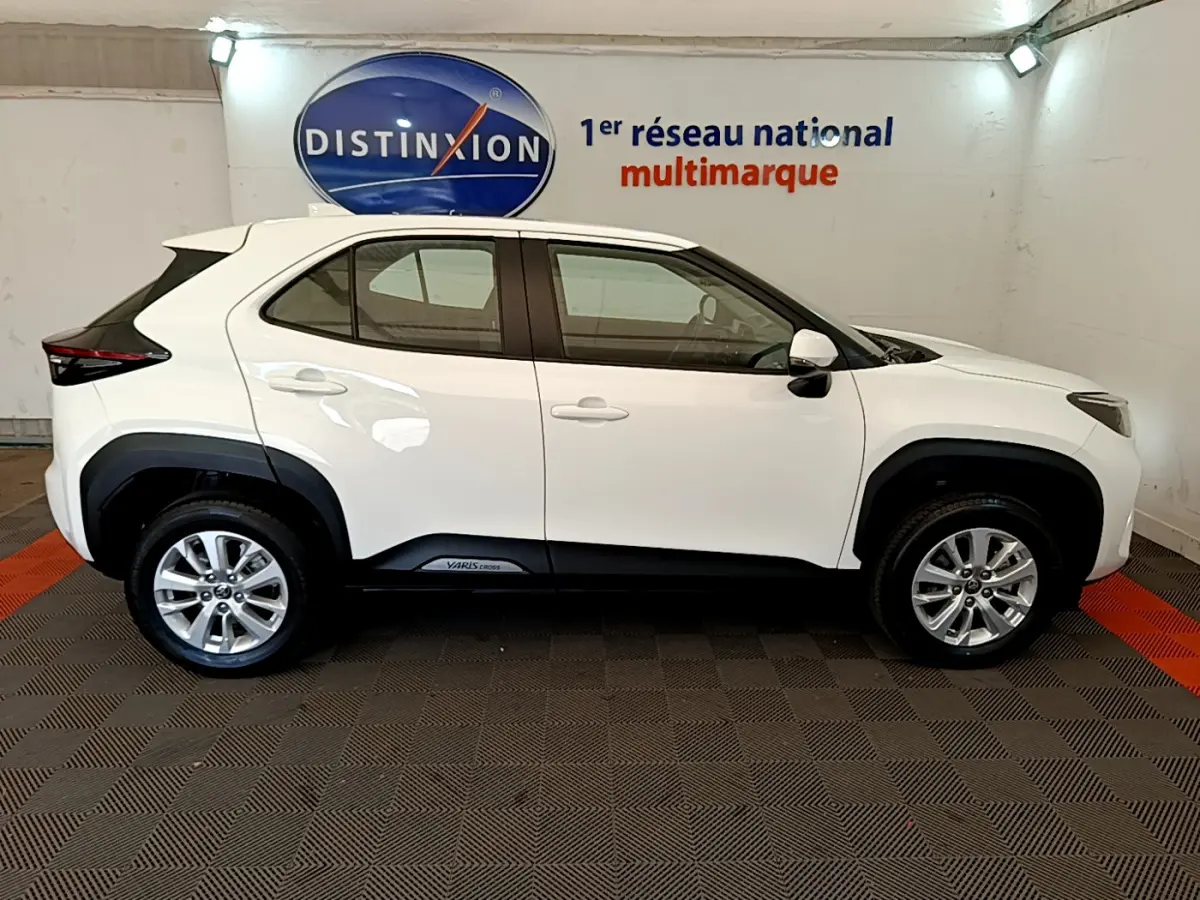 Profil côté gauche d'un Toyota Yaris Cross blanc 2022 avec jantes alliage et protections noires sur les passages de roues.