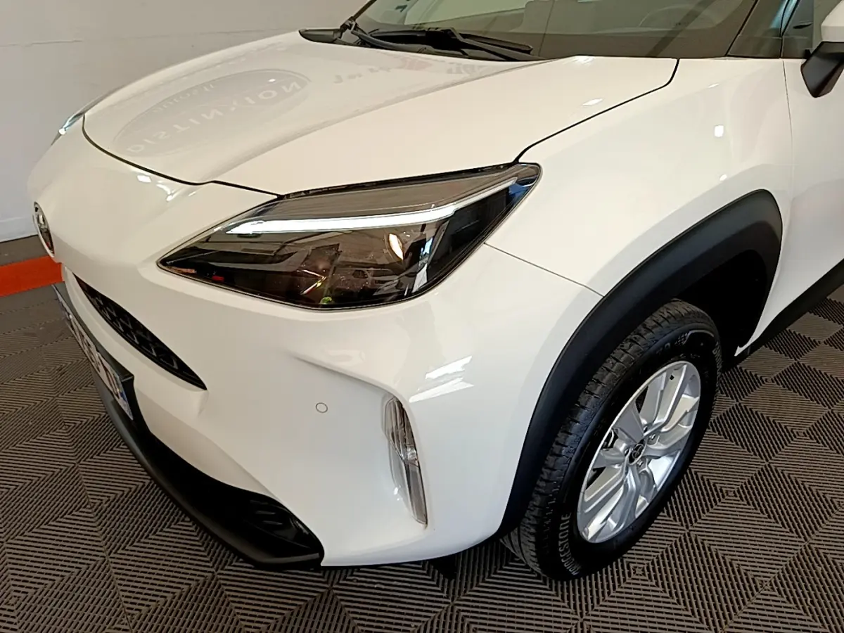 Vue 3/4 avant droit d'une Toyota Yaris Cross blanche avec phares LED et protections noires sur les passages de roues.