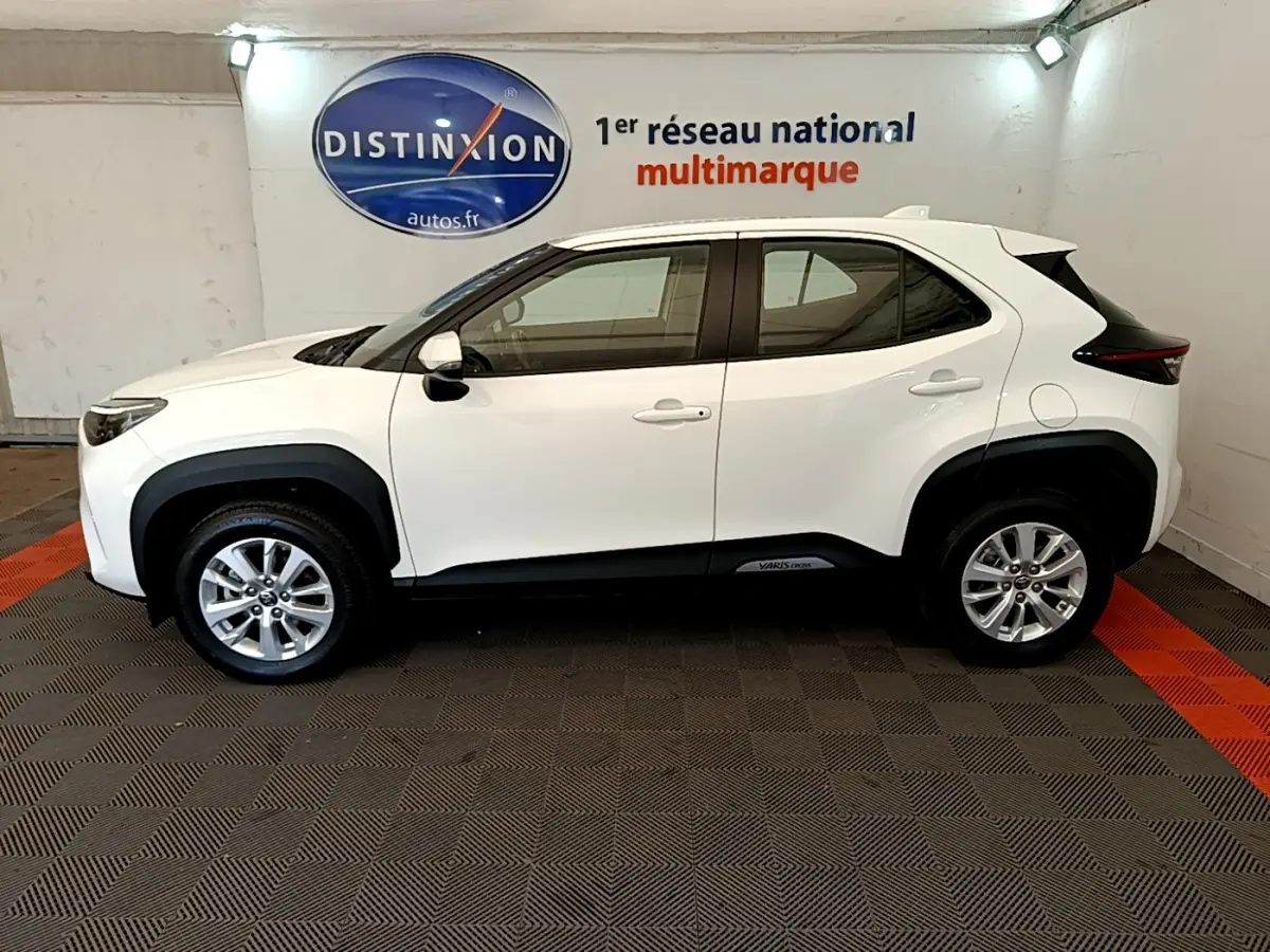 Profil droit d'une Toyota Yaris Cross blanche 2022 avec protections noires et jantes alliage visibles en intérieur showroom.