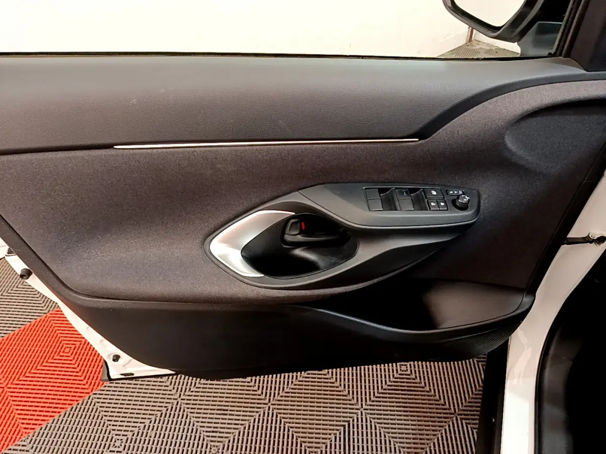 Intérieur côté gauche de la porte avant blanche de la Toyota Yaris Cross 2022 avec commandes de vitres et poignée noire.