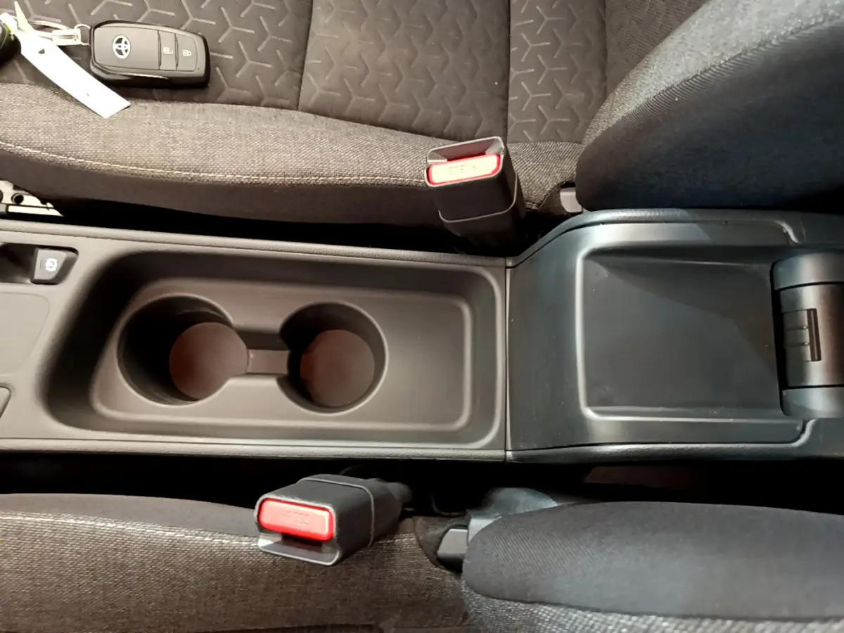 Vue plongeante sur la console centrale noire avec porte-gobelets et sièges tissu gris de la Toyota Yaris Cross blanche hybride 2022.