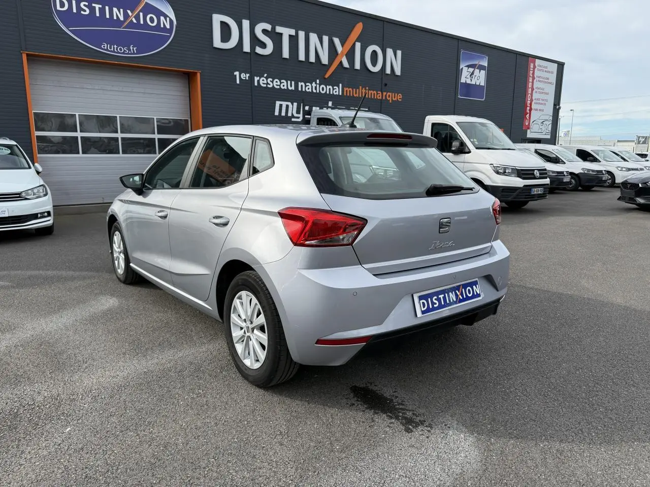Vue 3/4 arrière droite d'une SEAT Ibiza 1.0 TSI argent Urban avec jantes alliage 15'' sur parking de concession.