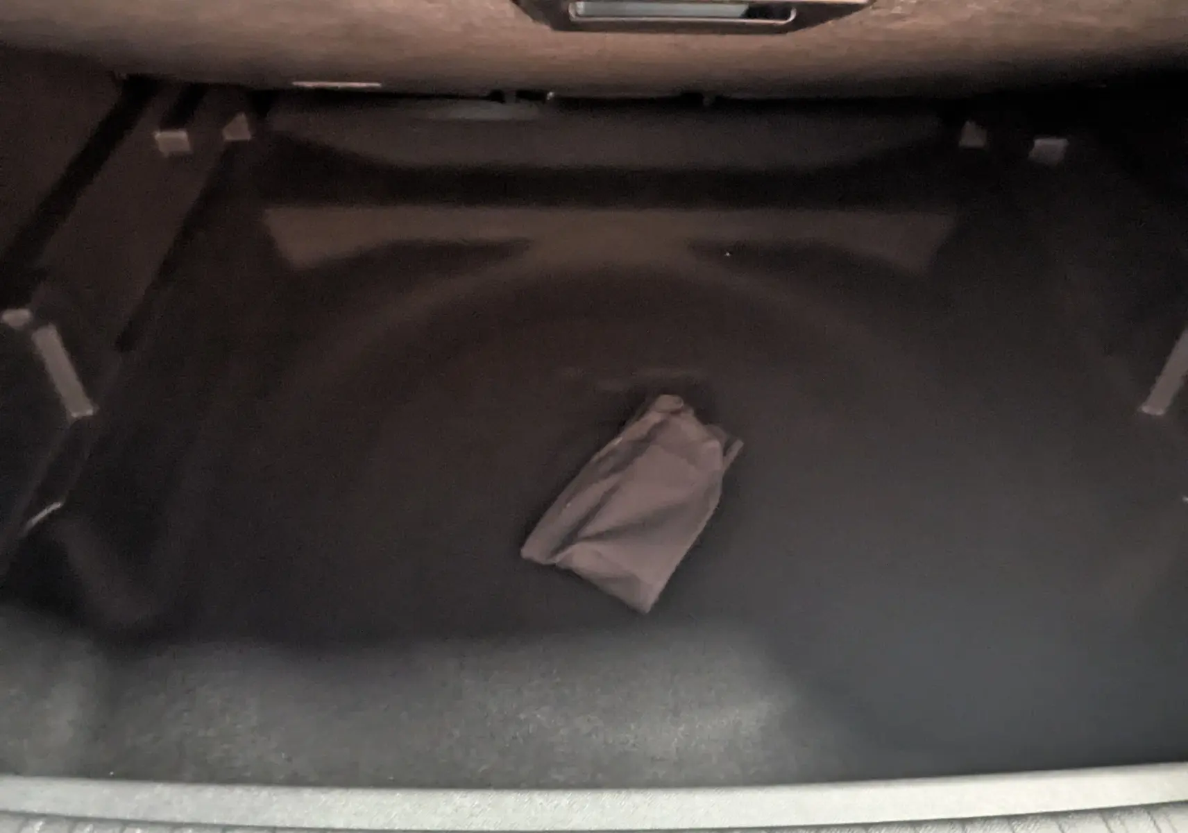 Coffre arrière vide du Peugeot 3008 Hybrid 145 GT, vue plongeante sur la moquette noire avec un petit sac gris au centre.