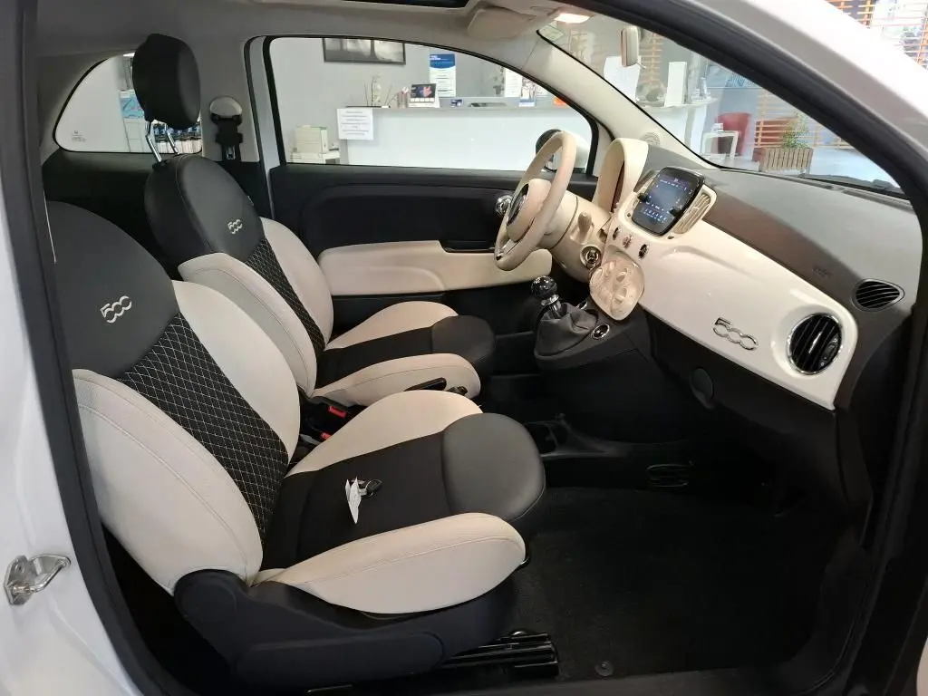 Vue intérieure côté conducteur de la FIAT 500 Dolcevita 2022 en Bossa Nova White, sièges bicolores noirs et beige avec logo 500 brodé.