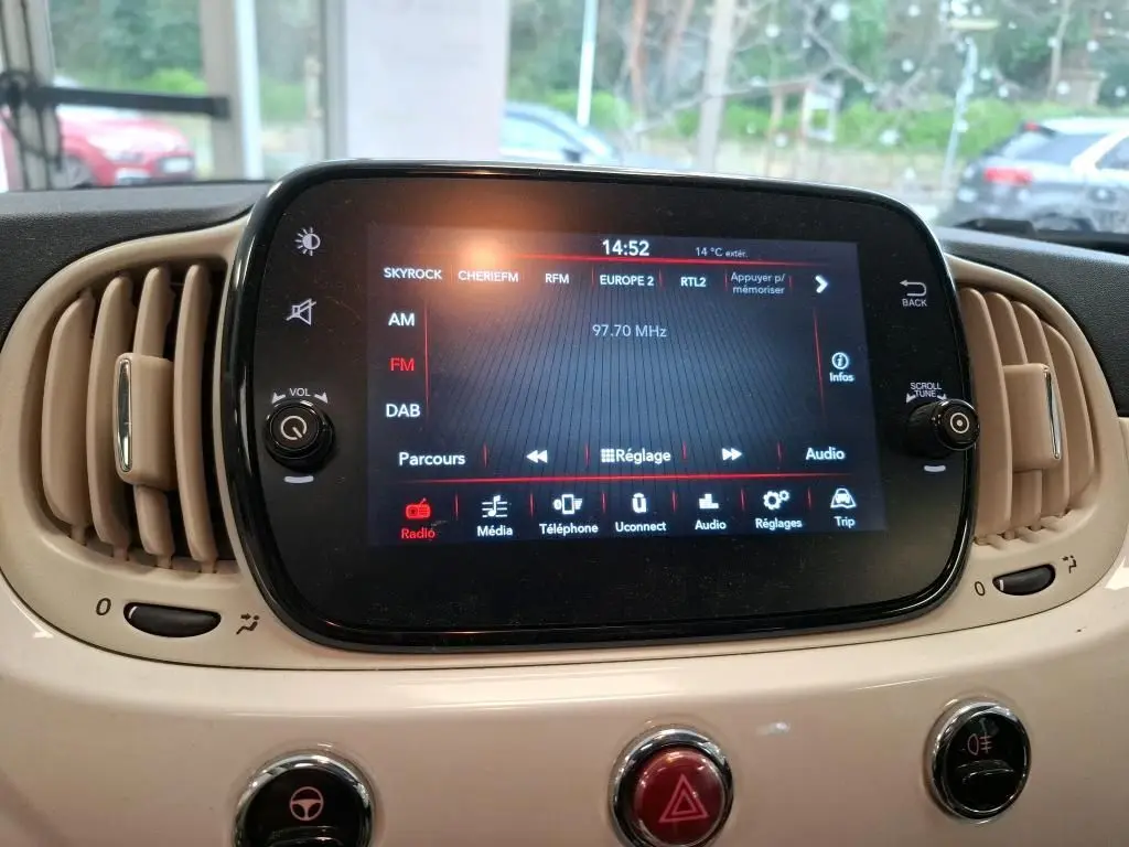 Écran tactile central du tableau de bord beige d'une Fiat 500 blanche, affichant la radio FM à 97,70 MHz.