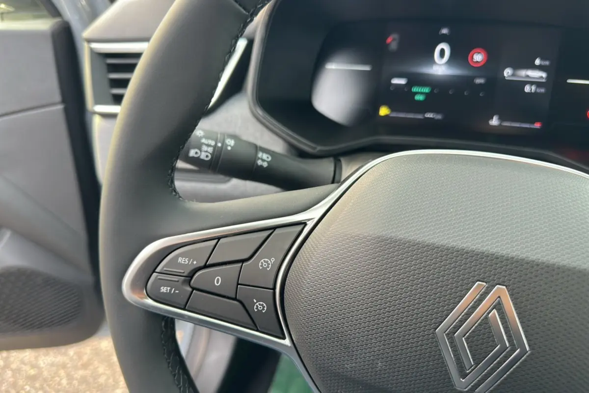 Gros plan sur le volant cuir multifonctions de la Renault Clio DCI 100 Evolution, tableau de bord numérique en arrière-plan.