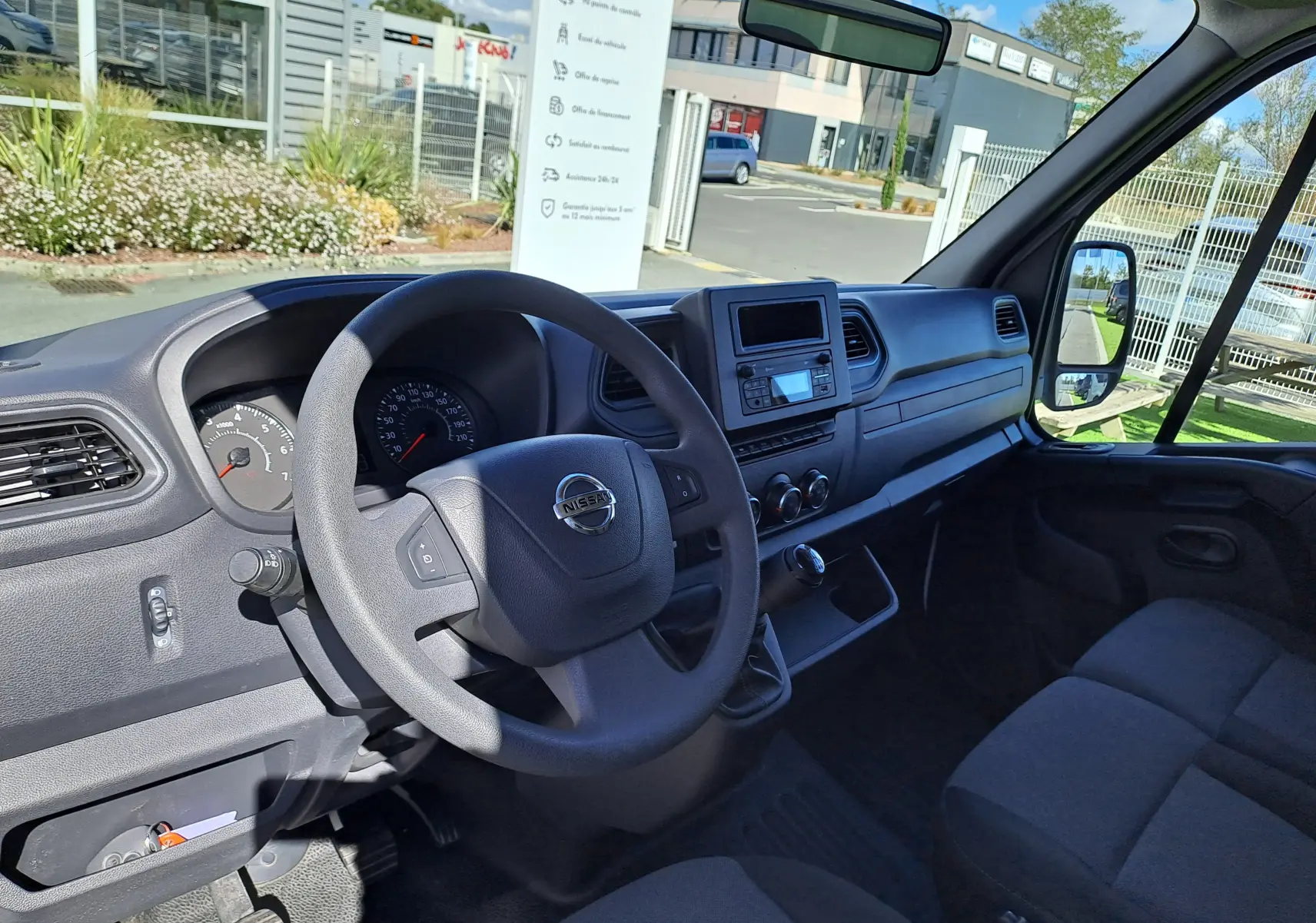Vue intérieure côté conducteur du Nissan Interstar blanc 2024, montrant le volant, tableau de bord et console centrale.