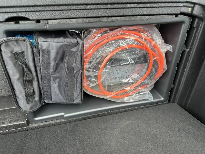 Rangement dans le coffre du Peugeot 3008 Hybride Rechargeable 2024, câble de recharge orange et sac noir visibles.