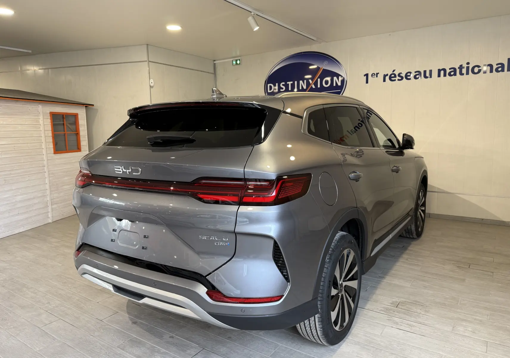 Vue 3/4 arrière droite du BYD SEAL U gris métallisé avec feux arrière LED et toit noir en intérieur showroom.