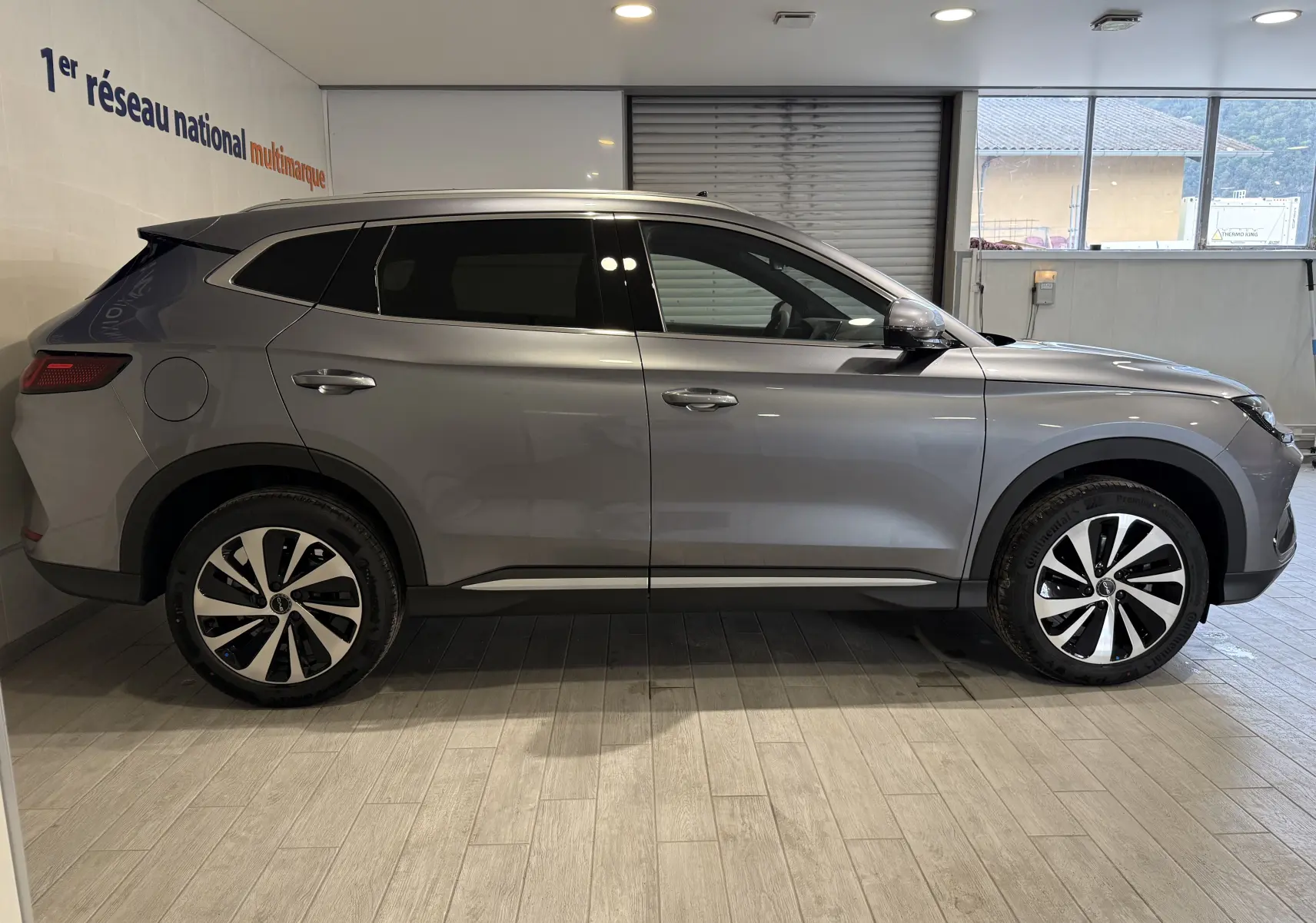 Vue de profil côté gauche d'un SUV BYD SEAL U gris métallisé avec jantes bicolores et vitres teintées, en intérieur showroom.