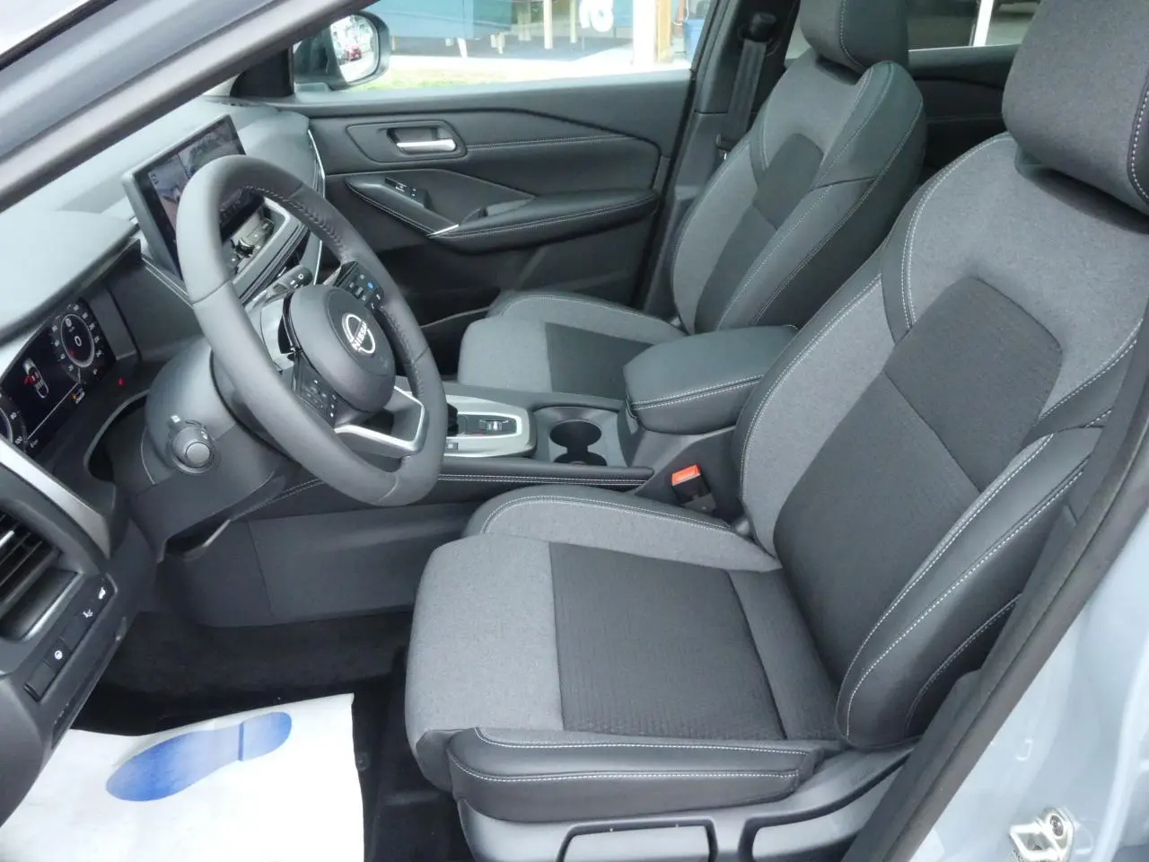 Vue intérieure côté conducteur du Nissan Qashqai 1.5 e-Power 2025, sièges gris bi-ton et volant cuir.