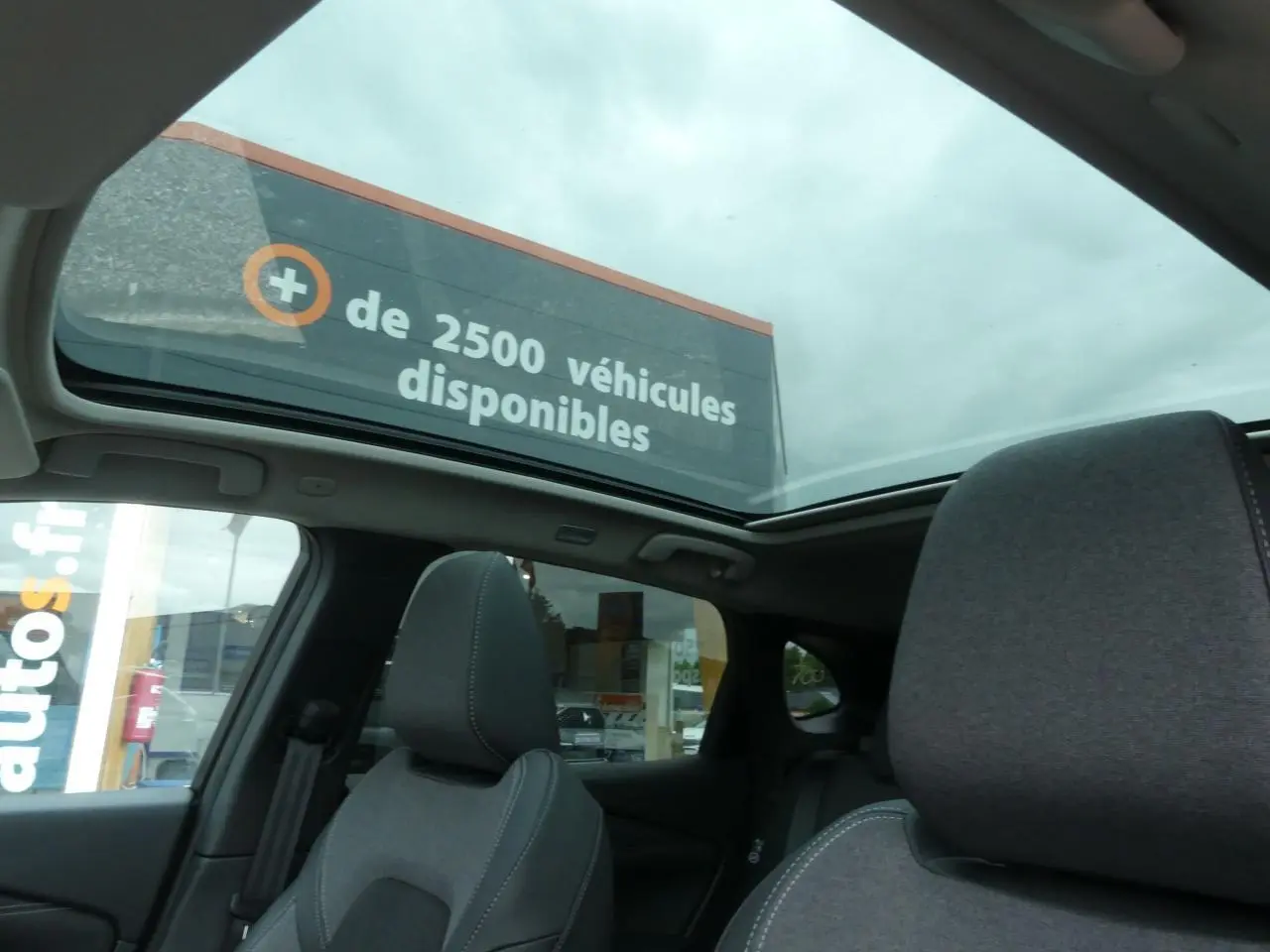 Toit panoramique ouvert montrant l'intérieur gris foncé du Nissan Qashqai 2025 côté arrière sous ciel nuageux.