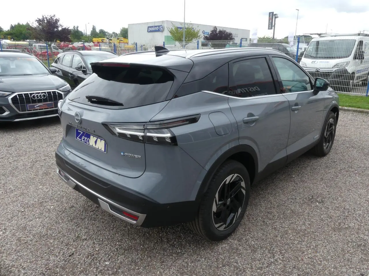 Vue 3/4 arrière droite du Nissan Qashqai gris métallisé avec toit noir et jantes alliage noires au stationnement.