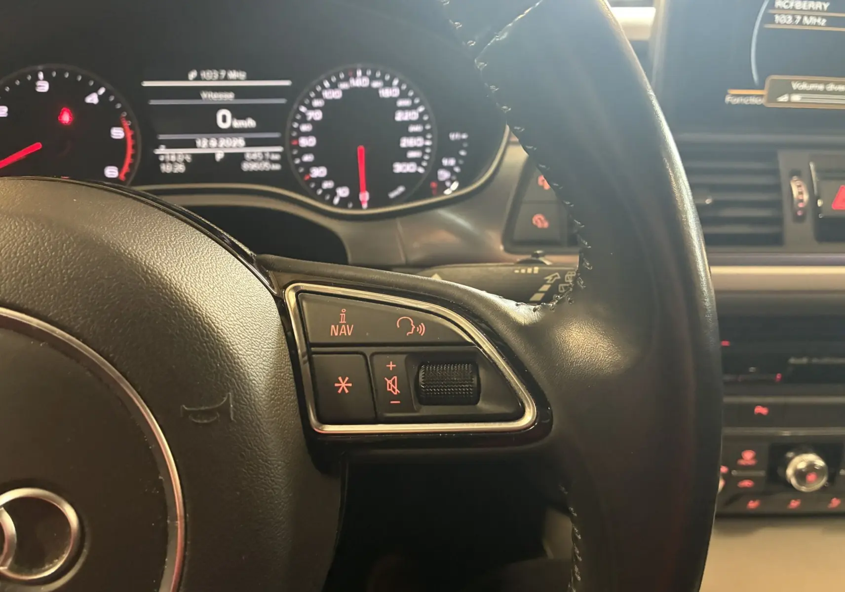 Gros plan sur le volant noir de l'Audi A6 Avant 2017, avec commandes audio et tableau de bord lumineux en arrière-plan.