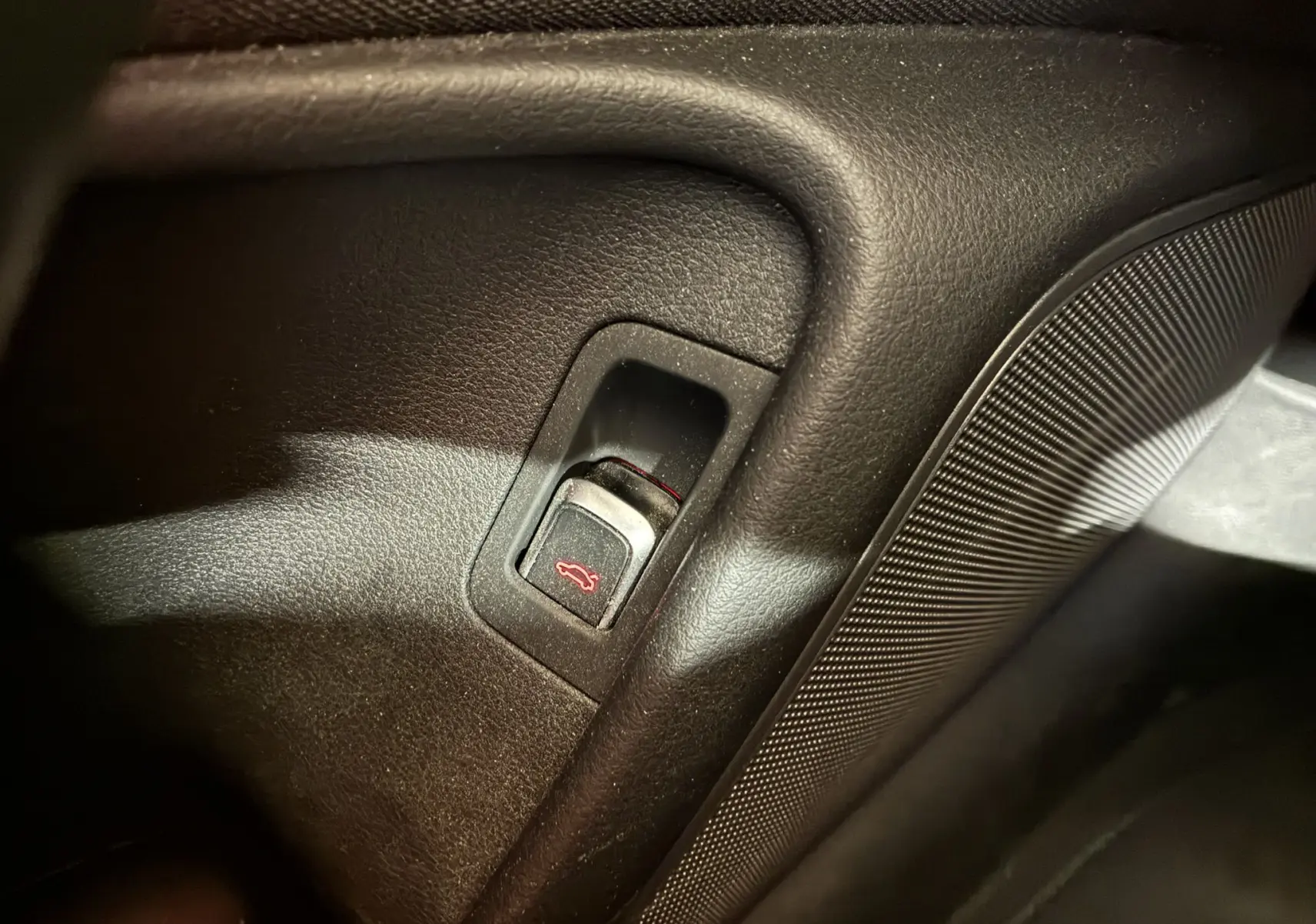 Bouton d'ouverture du hayon rouge sur panneau intérieur noir de l'Audi A6 Avant 2017 côté conducteur.