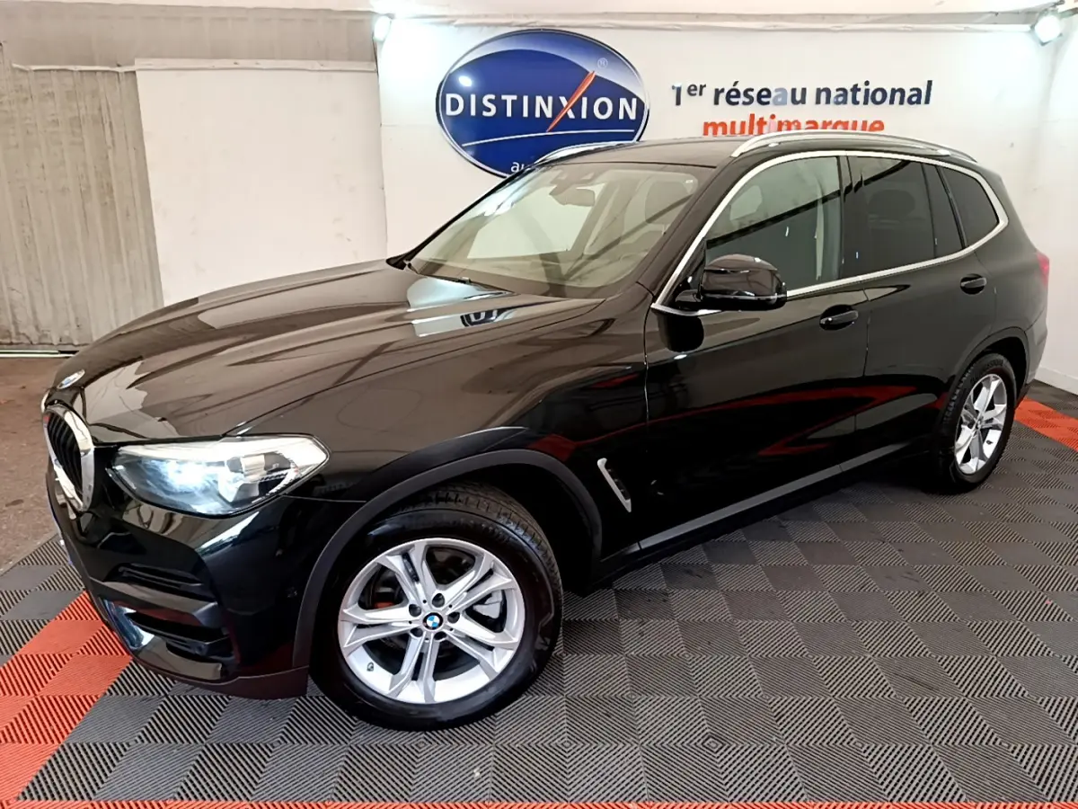 BMW X3 xDrive20d noir en 3/4 avant droit, avec jantes alliage et phares LED allumés dans un showroom.